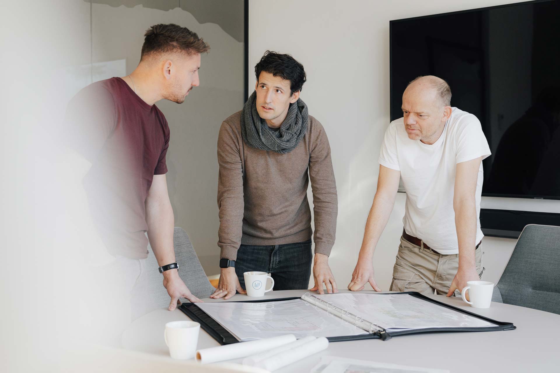 Drei Kollegen in einer Besprechung, während sie Pläne durchsehen.